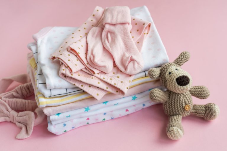 Baby  crocketed toy of dog  next to a stack rompers for kids